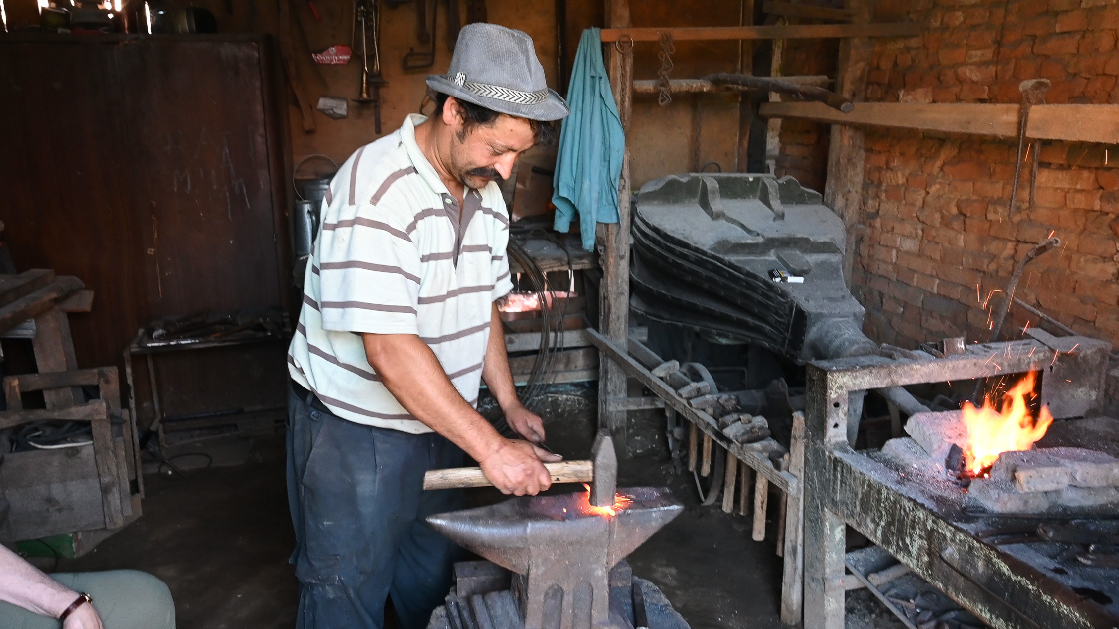 The blacksmith demonstrates his craft as he fashions a small horseshoe from a metal rod.